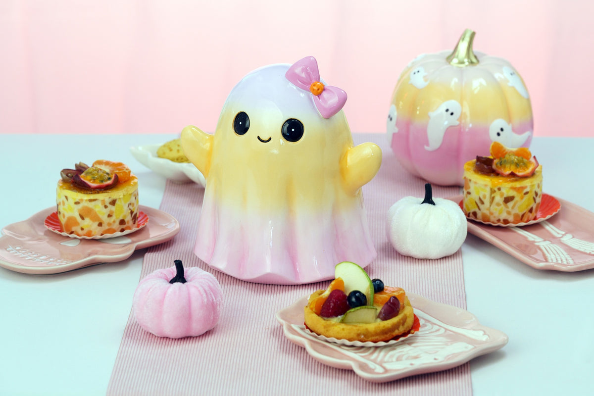 Fantôme décoratif dégradé jaune et rose près d'une citrouille à fantômes, ambiance d'Halloween pastel