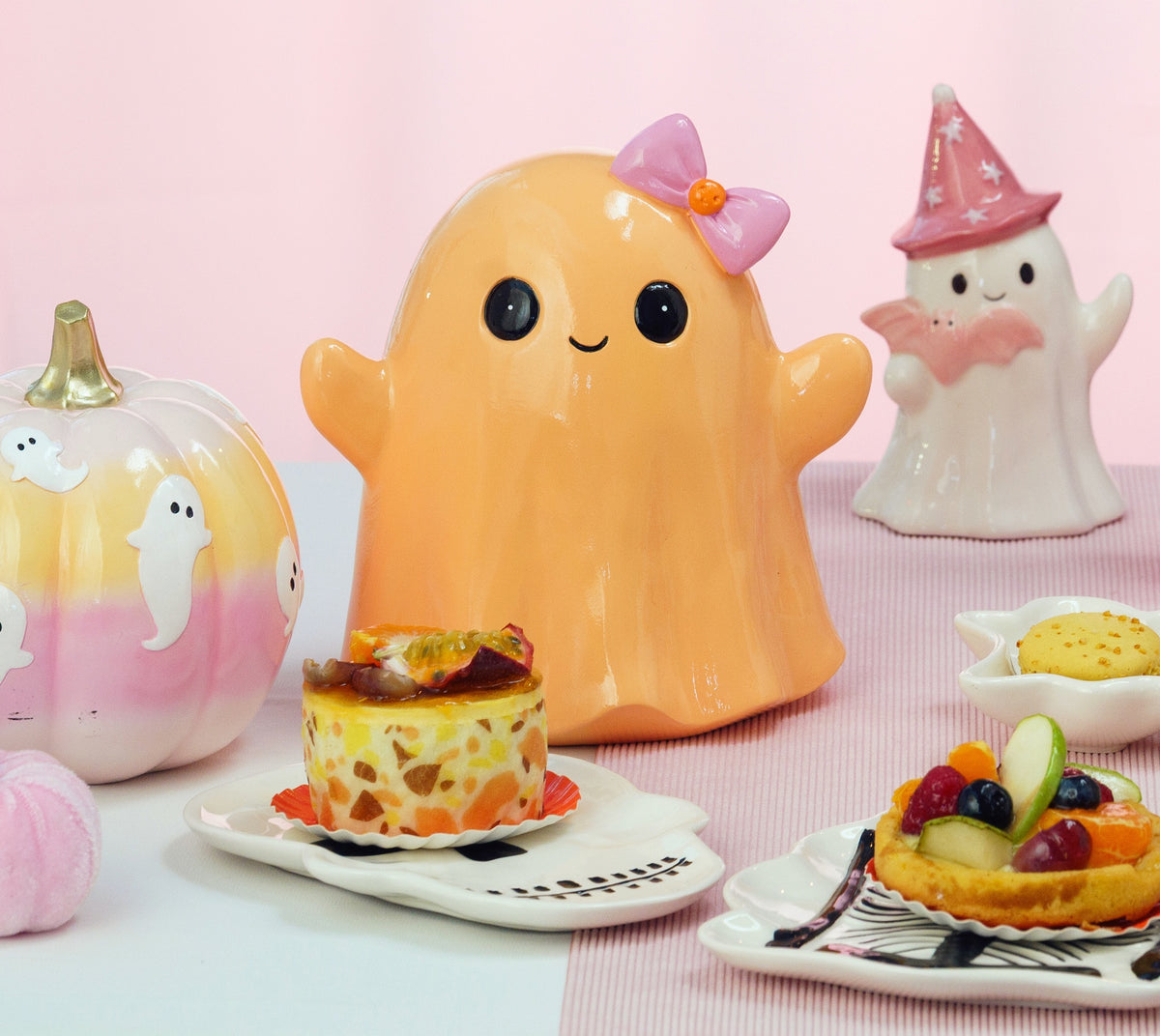 Fantôme Halloween souriant orange pastel à nœud rose, posé sur une table de goûter d'Halloween