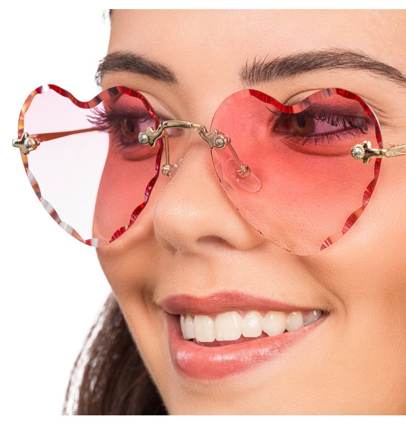 The image shows a pair of novelty party glasses with heart-shaped pink lenses and metallic arms.