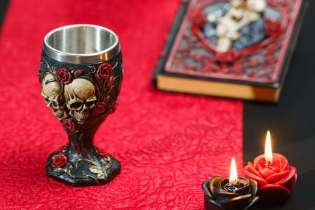 Calice gothique à crânes et roses posé sur un chemin de table rouge avec bougies, ambiance d'Halloween sombre