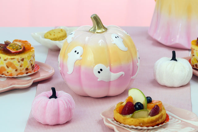 Citrouille Halloween dégradé pêche et rose ornée de fantômes, en scène sur une table pastel d'Halloween