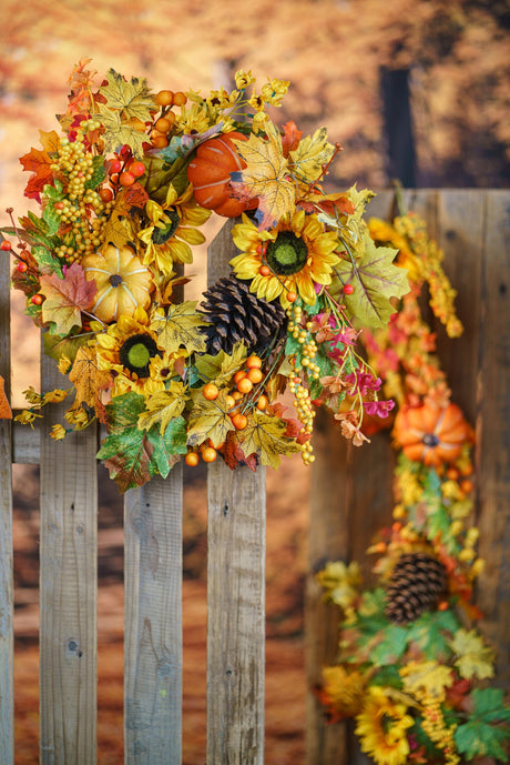 Couronne d'automne à tournesols et citrouilles avec guirlande de feuilles sur une clôture en bois