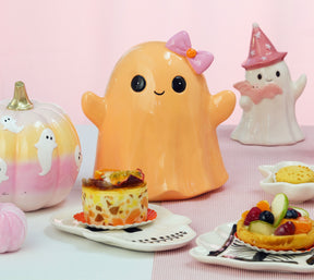 Fantôme Halloween souriant orange pastel à nœud rose, posé sur une table de goûter d'Halloween