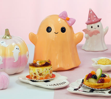 Fantôme Halloween souriant orange pastel à nœud rose, posé sur une table de goûter d'Halloween