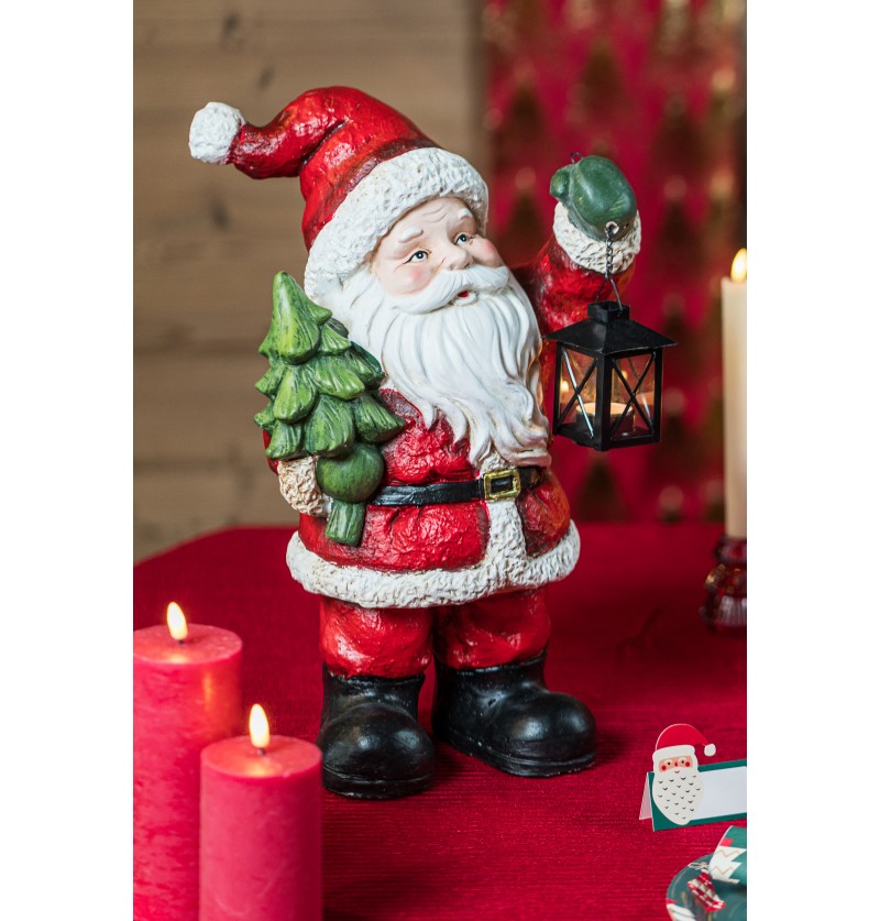 The image shows a decorative Santa Claus figure holding a Christmas tree and a metal lantern, designed as a festive ornament.